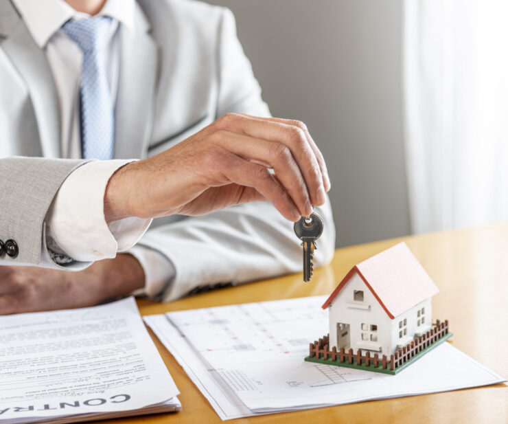 person-holding-house-keys-toy-model-house-desk