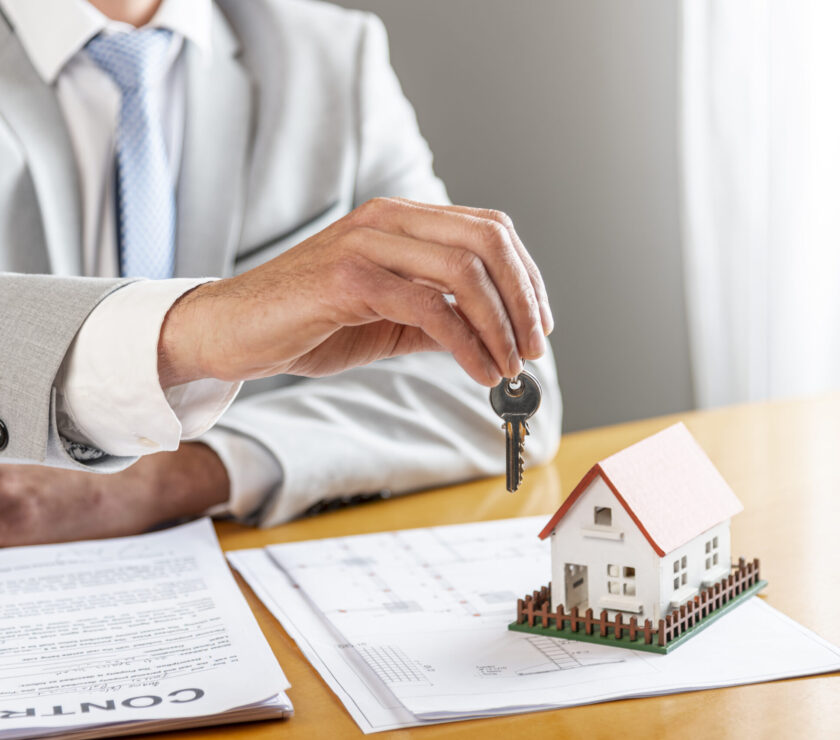 person-holding-house-keys-toy-model-house-desk